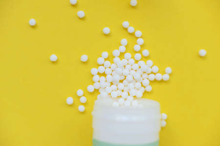 Homeopathic globules and with a plastic jar on a yellow background. Alternative Homeopathy medicine...