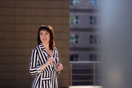 modern photographer happy girl in a leather cut for the camera against the backdrop of skyscrapers. woman wearing a blue shirt, black shorts and white trendy sneakers space for textの写真素材