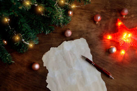 wish list New Year's Eve with a ballpoint pen on a wooden background under a Christmas tree with garlands and beautiful balls. festive composition. Flat lay, place for text. letter to santa.の写真素材