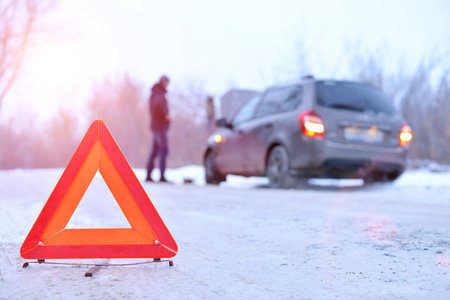 car repair on the road in winter. a young man is trying to fix a car breakdown under the soot on the road. woodsroadside assistance carの写真素材