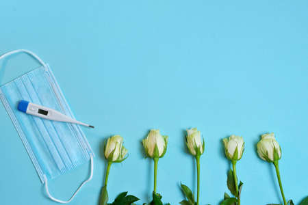 white roses, medical mask, thermometer thermometer, on a blue background. Doctor's Day concept, flat...