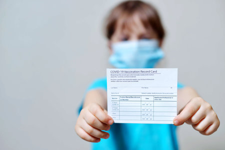 girl is holding a vaccination record card and corona virus vaccine vials. Passport of immunity to the coronavirus in the hands of a child. Health passport as proof of recovery from COVID-19.の写真素材