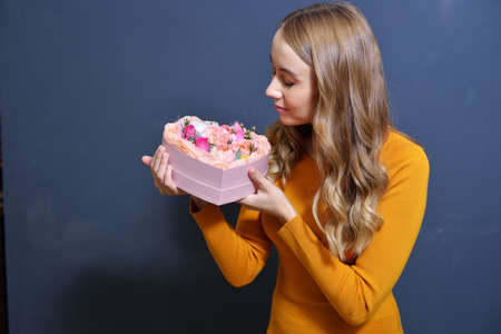 happy young blonde girl in a light gray sweater holds a bouquet of flowers in her hands on a dark gray monochrome backgroundの写真素材