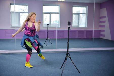 banner A blonde dancer blogger girl leads online dance fitness courses via phone during a pandemic. Online learning conceptの写真素材