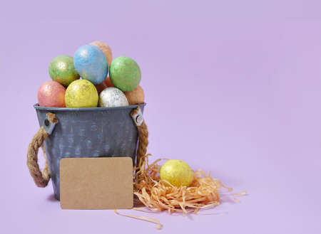 Colorful Easter eggs on a soft purple background in a gray bucket in the style of minimalism. with...