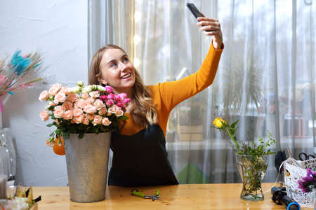 Florist woman creates flower arrangement. Small flower shop. European floral shop concept. Flowers delivery. Handsome fresh bunchの写真素材