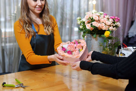 Floral shop concept. Florist woman Floris woman gives a heart-shaped box with flowers for delivery....
