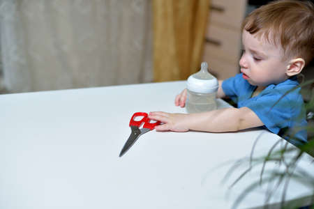 Danger in the home, sharp objects are dangerous for young children. little boy picks up scissors...