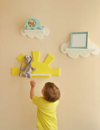 Stylish and modern Interior design. Home for the child room. todder boy takes a gray hare's soft toy from the shelfの写真素材