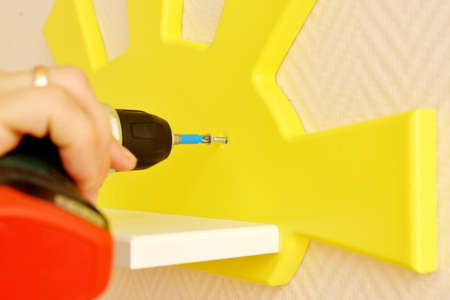 Stylish and modern Interior design. Home for the child room. close-up of a man screwing a frame in the form of a yellow sun to the wall with a screwdriver. home improvement and comfort.の写真素材