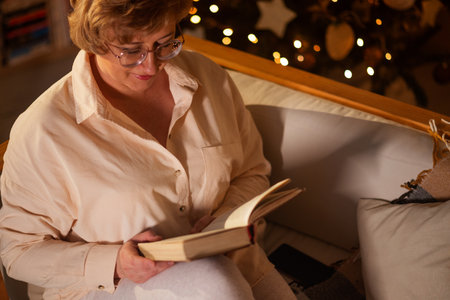 woman reads a book on christmas night. christmas, comfort, leisure and people concept - happy woman reading book in bed at home bedroom family Christmas traditions.の写真素材