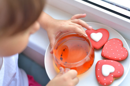 A girl in a white T-shirt holds a cup of tea and a liver in the form of a red heart. delicious sweet snack concept.の写真素材