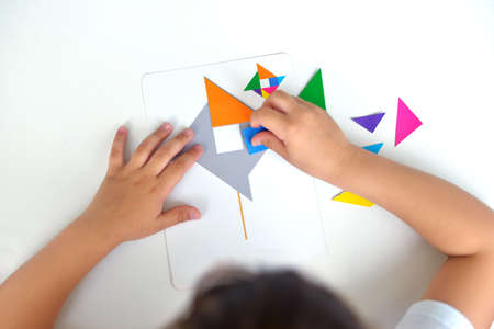 A preschooler girl sitting at the table collects a drawing from a geometric figure. the concept of early childhood development by montessori. a game of logic and imagination.の写真素材