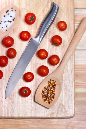 Fresh vegetables - tomato cherry and knife on wooden board on table background. Top view. Healthy food concept. The process of cookingの写真素材