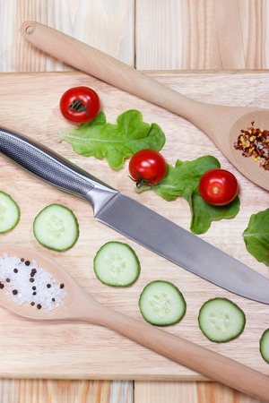 Sliced cucumber,cherry tomatoes, spice on wooden cutting board.Healthy food concept.The process of cookingの写真素材