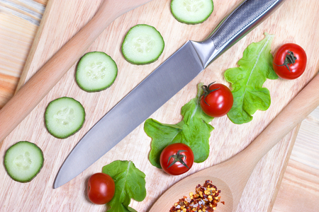 Sliced cucumber,cherry tomatoes, spice on wooden cutting board.Healthy food concept.The process of cookingの写真素材