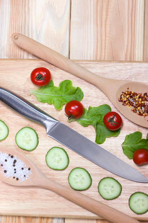 Sliced cucumber,cherry tomatoes, spice on wooden cutting board.Healthy food concept.The process of cookingの写真素材