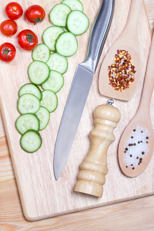Sliced cucumber,cherry tomatoes, spice on wooden cutting board.Healthy food concept.The process of cookingの写真素材