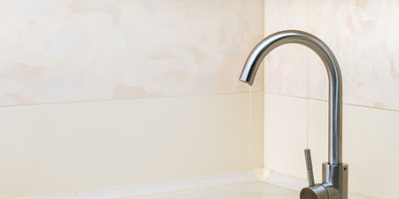 water flows from the tap in a thin stream. broken faucet on white beige background with copy space. Concept of saving water.の写真素材