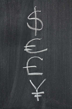 Dollar, pound, yen and euro symbols, sketched with white chalk on a black boardの写真素材