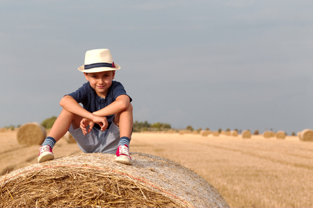 A cute boy is sitting on a haystack.Active outdoors with children on warm summer day.Summer concept, a vacation.の写真素材