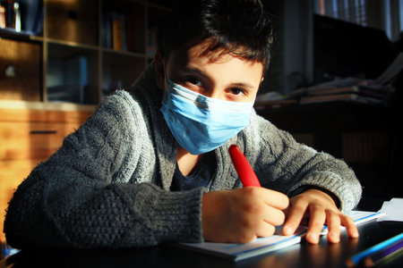 Teenager boy wearing face mask doing homework at home and writing notes.の写真素材