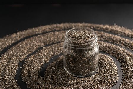 Small jar with chia seeds on black background. Copy space. Chia superfood paleo diet concept.の写真素材