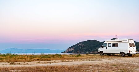 Caravan on the beach with pink sky during sunset. Motorhome tourism concept. Space for textの写真素材