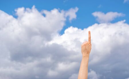 Female raised hand pointing finger in the air with sky and clouds on background. Idea concept. Copy space.の写真素材