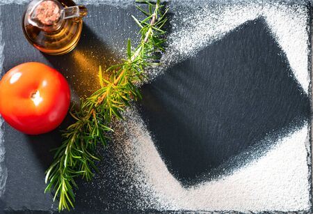 Flat lay mockup made with flour on stone board, with tomato, olive oil and rosmarine. Cooking concept. Copy space, view from top.の写真素材