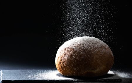 Close up bread with falling flour on black background. Bread making concept, copy space, horizontal.の写真素材