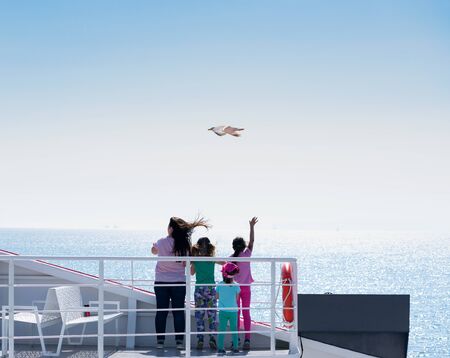 Unrecognisable family standing on the cruise ship deck waving and enjoying the view of the sea....
