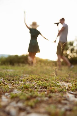 Silhoette of couple walking at field holding hands while man photoshooting a woman. Selective focus