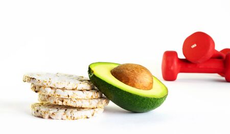 Staked crunchy rice cakes and half of avocado with unfocused red dumbbells on background. Helthy...