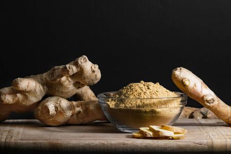 Ginger powder in glass bowl on wooden cutting board with ginger roots and slices. Healthy eating concept.の写真素材