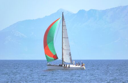 Sailing yacht with colorful sail in open sea at day with island at background. Yachting adventure conceptの写真素材