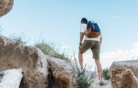Back biew of caucasian tourist man with backpack climbing rocky mountain.の写真素材