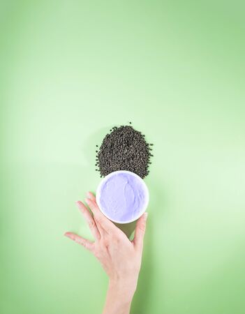 Woman's hand holding purple moisturizing cream with bakuchiol ingredient. Babchi seeds (Psoralea corylifolia). Bakuchiol cosmetics concept. Flat lay, copy space, vertical.の写真素材