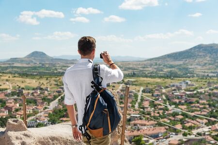 Man tourist with backpack taking pictures or footage with action camera on top of Uchisar castle.の写真素材