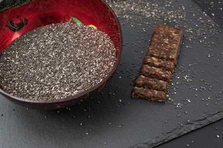 Bowl of dry chia seeds and protein bar on stone board with black background. Protein source superfood concept.の写真素材