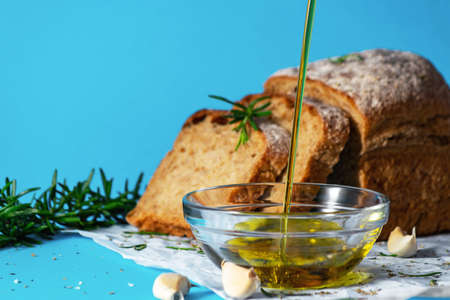 Olive oil pourin into a saucer close up with bread and herbs on bakcground. Mediterranean cuisine concept. Healthy eating habits. Gmo free.の写真素材