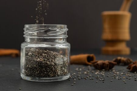 Pouring dry chia seeds in glass jar with unfocused objects on background. Copy space. Paleo diet, chia superfood concept.の写真素材