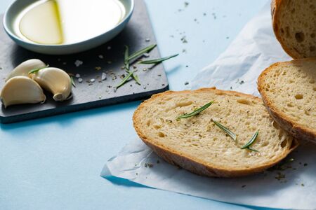 Close up slices of bread with rosmarine and saucer with olive oil on papyrine on blue background. Gluten free healthy eating concept. Mediterranean cuisine.の写真素材