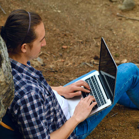 Man sitting on ground at forest and working on laptopの写真素材