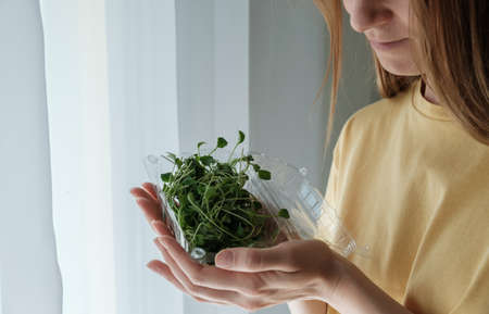 Woman holding plastic container with edible broccoli sprouts.