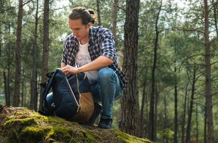 Young active man with backpack at forest during sunny day.