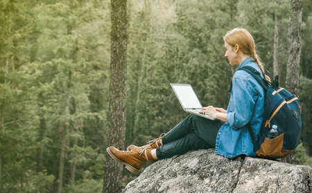 Young woman sitting on ground at forest and working on laptop .