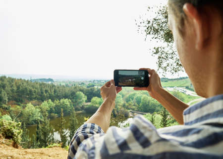 Man taking photo of landscape on smartphone.の写真素材