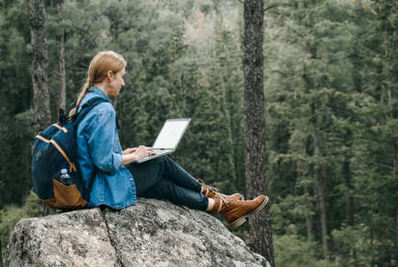 Young woman sitting on ground at forest and working on laptop .の写真素材