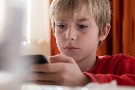 Kid looking at smartphone during breakfast.